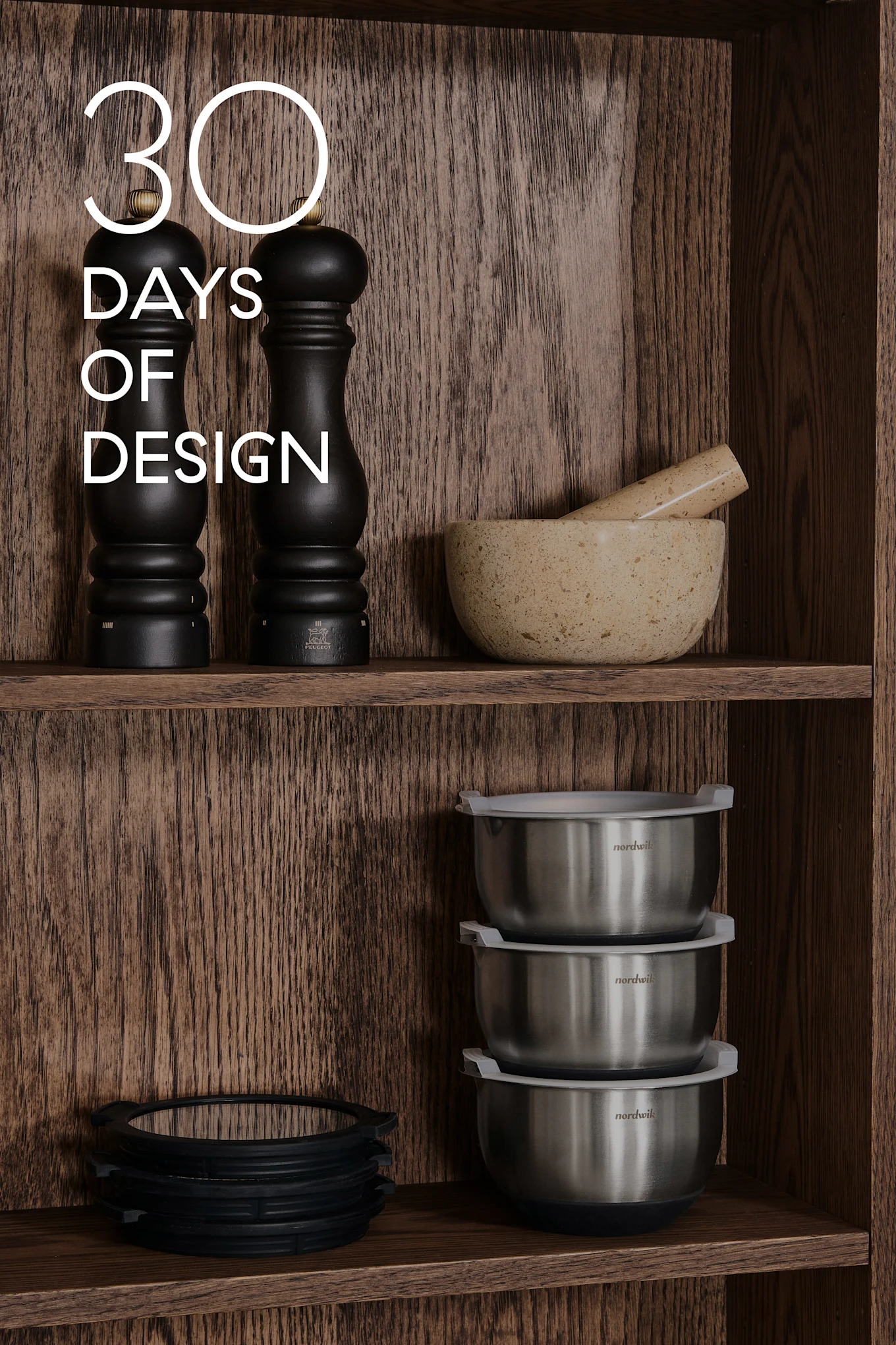 Holzregale mit Küchenutensilien: schwarze Mühlen, Mörser & Stößel, Stahlschüsseln, Silikonringe. Text: 30 DAYS OF DESIGN.