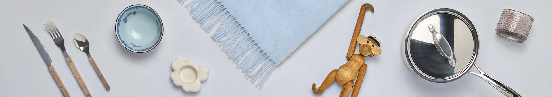 Sortiment von Haushaltswaren: Besteck mit Holzgriffen, eine blaue Schale, Blumenuntersetzer, blaue Decke, Holzaffe, Topf und Glas.