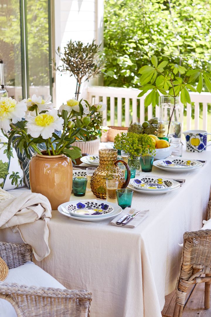 Decken Sie den Tisch für den Mittsommer in einem mediterran inspirierten Stil mit gelben Details, Pfingstrosen auf dem Tisch und grünen Gläsern von Iittala. 