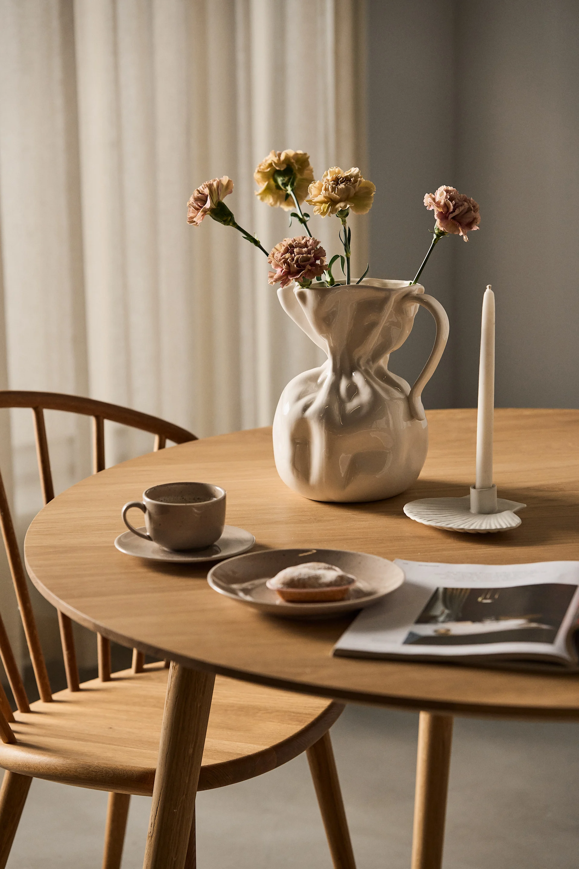 Auf einem Esstisch steht die weiße Crumple Vase von Byon mit einzelnen Schnittblumen.