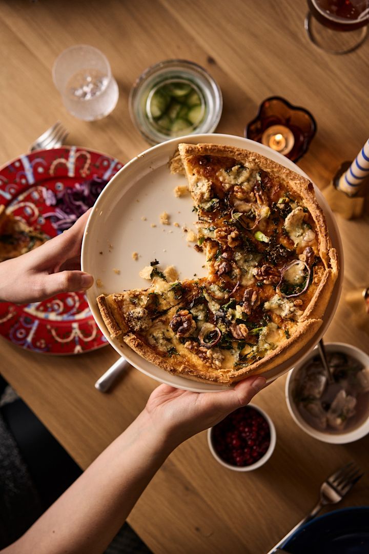 Schwedisches Weihnachtsessen: Hier sehen Sie eine Grünkohl-Quiche auf einem Teller, welche über den weihnachtlich gedeckten Tisch gereicht wird.