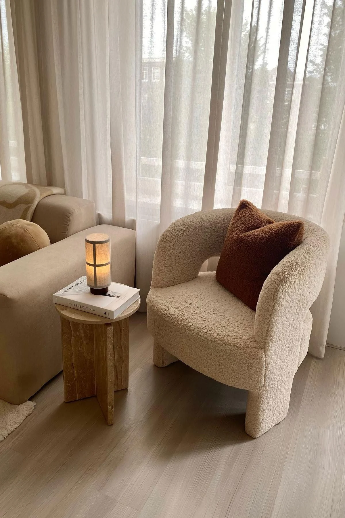 Auf einem Couchtisch aus Marmor liegt ein Buch, darauf steht die Hashira Tischleuchte von Audo Copenhagen, links davon eine Couch, rechts davon ein Sessel.