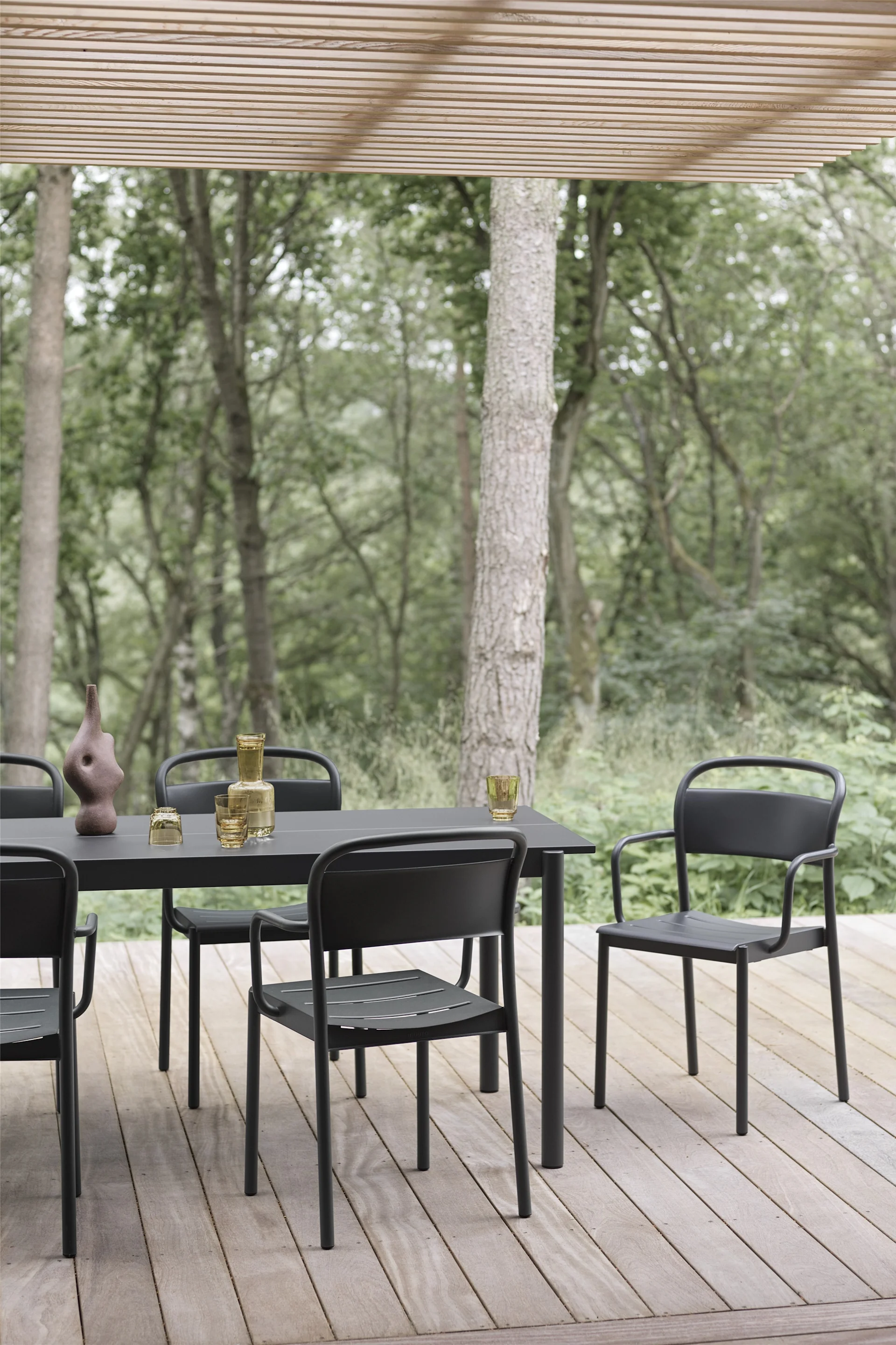 Eine überdachte Terrasse aus Holz, auf der ein Tisch und Stühle in Schwarz aus der Linear-Kollektion von Muuto stehen.