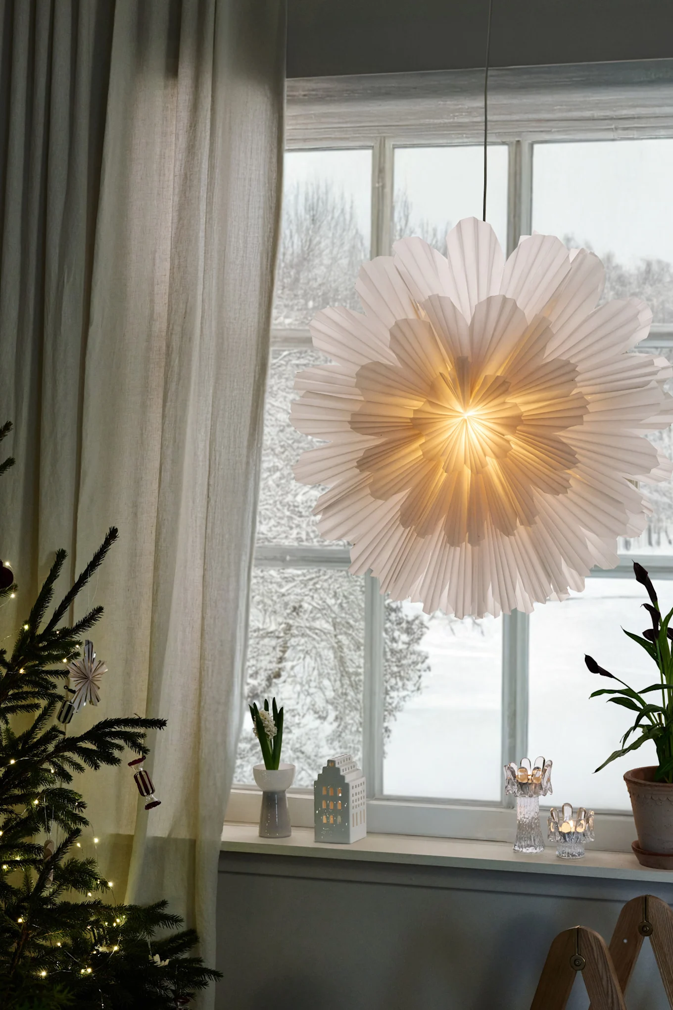 Weihnachtsdeko modern – hier sehen Sie den Weihnachtsstern aus Papier von Snöblomma, der in einem Fenster hängt und von hinten beleuchtet wird.