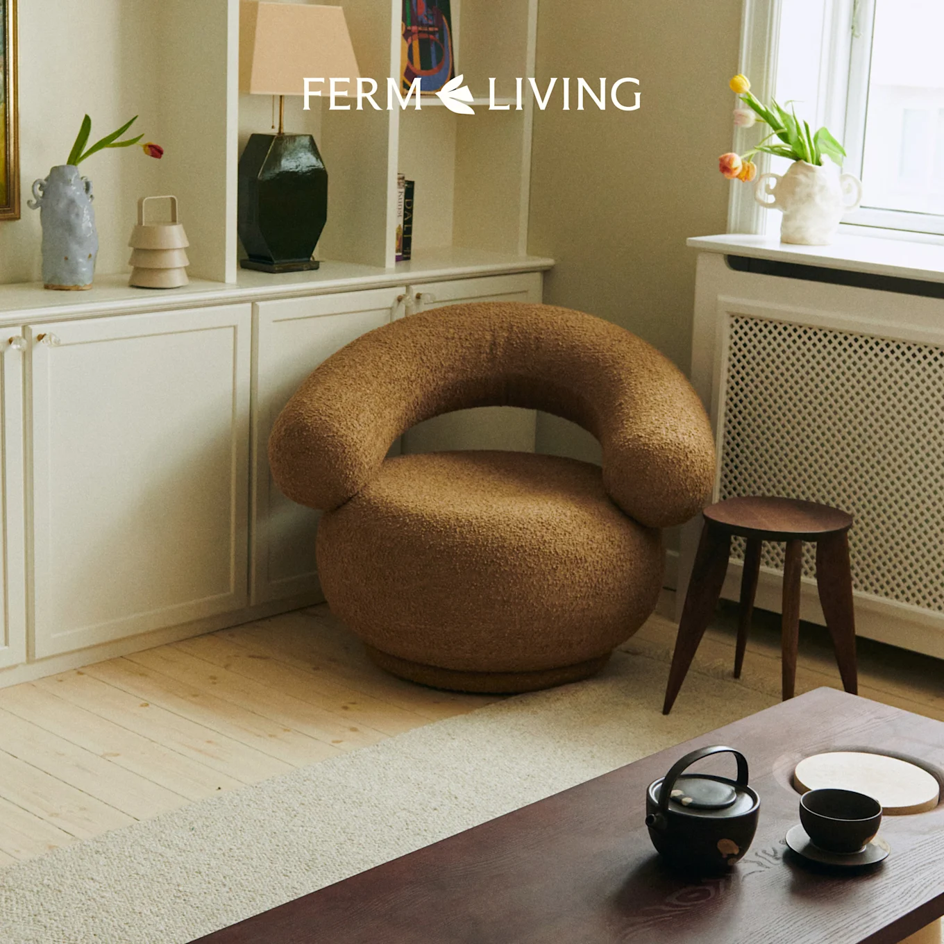 Ein gemütliches Wohnzimmer mit einem braunen, strukturierten runden Sessel, einem Holztisch mit Teeservice und einem weißen Schrank.