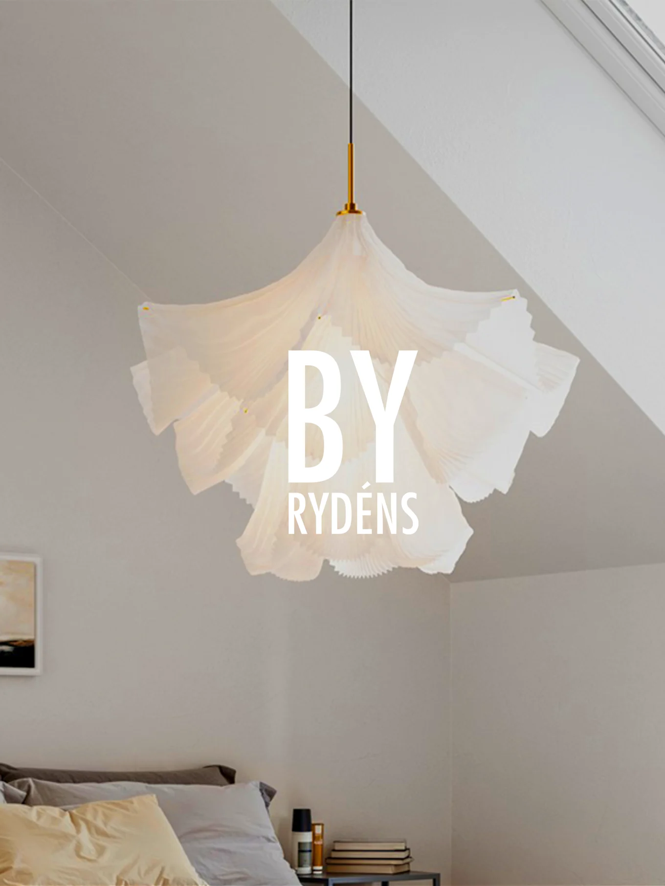 Eine weiße, plissierte Skulpturen-Pendelleuchte hängt über einem Bett mit Kissen und einem Nachttisch. 'BY RYDÉNS' ist über der Lampe eingeblendet.