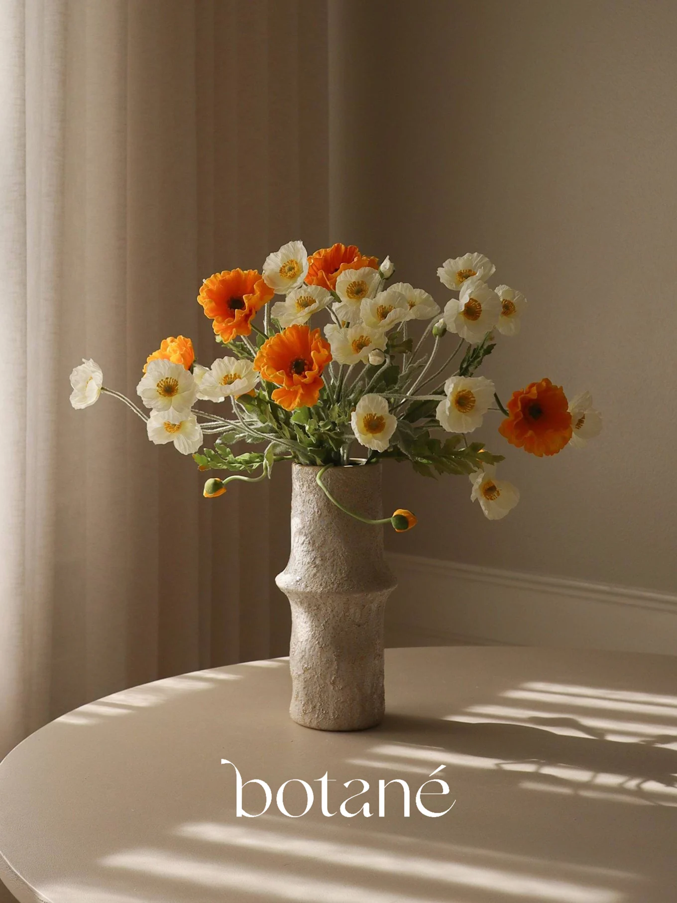 Eine texturierte Vase mit einem Strauß orangefarbener und weißer Kunstmohne auf einem Tisch mit Streifenschatten.