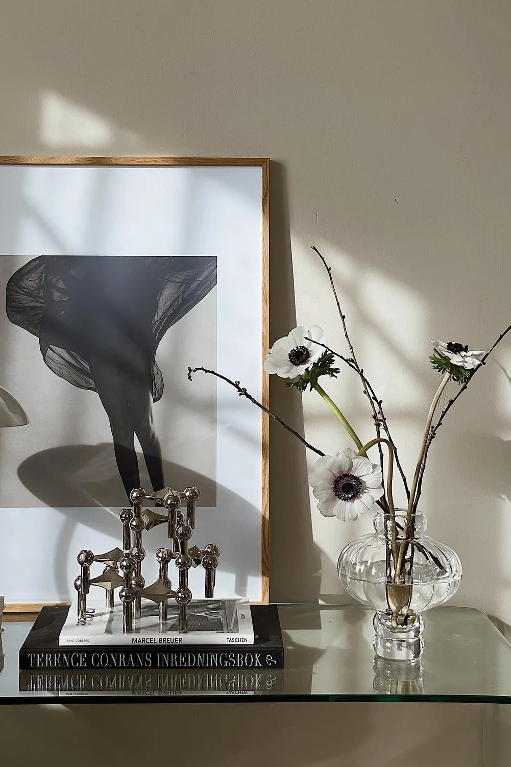 Gerahmtes Schwarz-Weiß-Foto von Beinen mit fließendem Stoff, modularem Kerzenhalter, Büchern und weißen Anemonen in Vase.