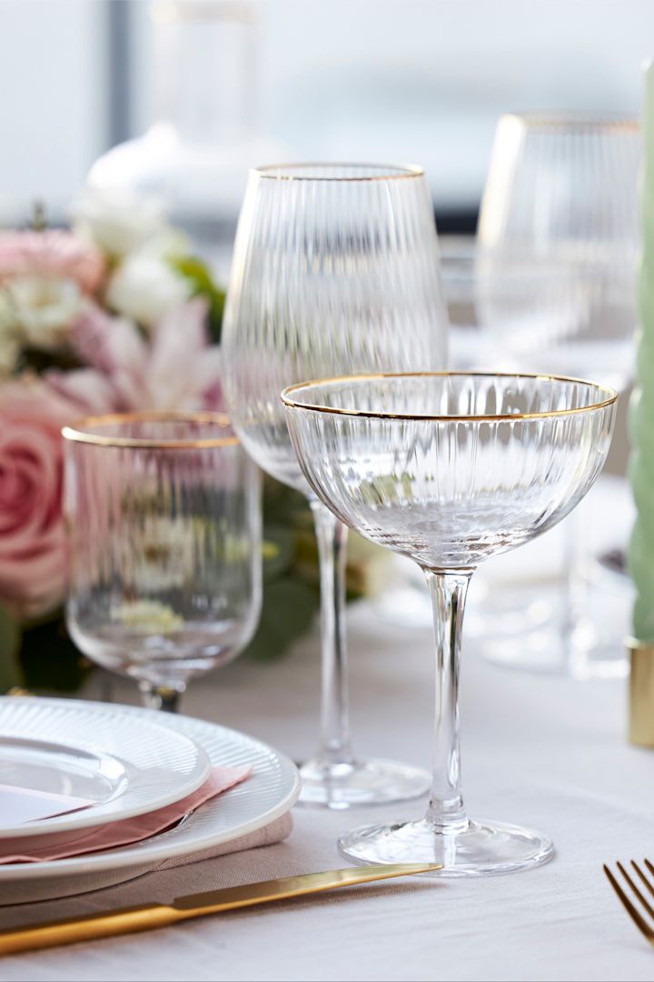 Die Gläser aus der Palermo-Kollektion von Lyngby Glas haben einen eleganten goldenen Rand und stehen hier auf einem stilvoll gedeckten Tisch in Weiß, Rosa und Gold.