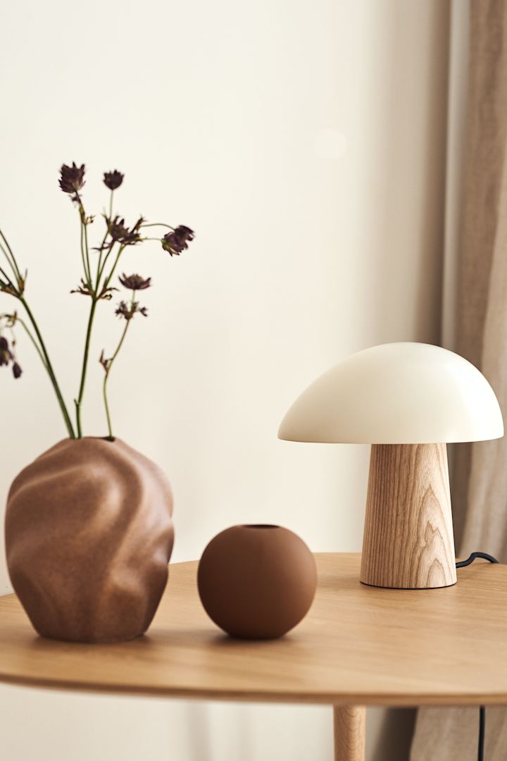 Dekorieren Sie Ihr Wohnzimmer mit beigen Möbeln und verschiedenen Beigetönen, um einen schönen Kontrast in Ihrem Zuhause zu schaffen. Hier sehen Sie die DriftVase und die Ball Vase von Cooee Design in kastanienbraunen Tönen zusammen mit der Tischleuchte Night Owl von Fritz Hansen in Weiß- und Beigetönen.