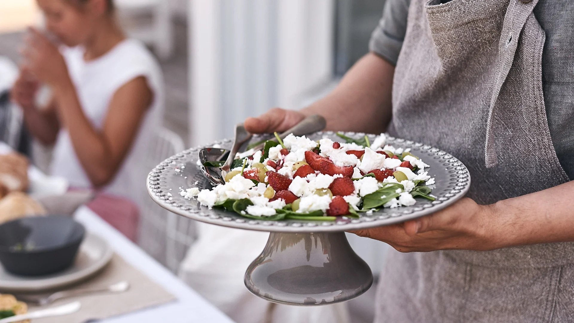 Auf dem sommerlich gedeckten Tisch wird auf einer Kuchenplatte von PotteryJo ein herrlich sommerlicher Salat mit Erdbeeren und Feta-Käse serviert.