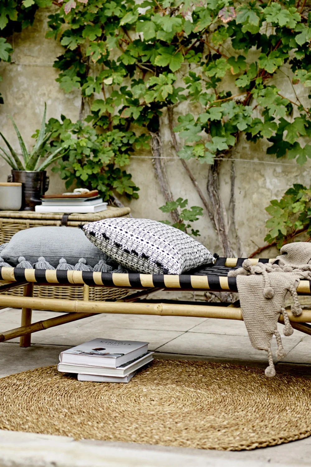 Dekorieren Sie mit Textilien, um einen Balkon im Boho-Stil zu dekorieren. Hier sehen Sie eine Liege auf einem Balkon, darunter liegt der Eternal Juteteppich von Ferm Living.