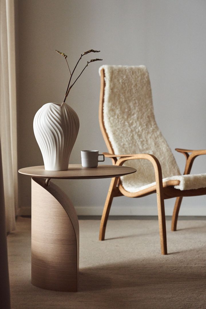 Hier sehen Sie den Savoa Tisch und den Lamino Sessel mit weißem Schaffell und Eichenholz der schwedischen Möbelmarke Swedese.