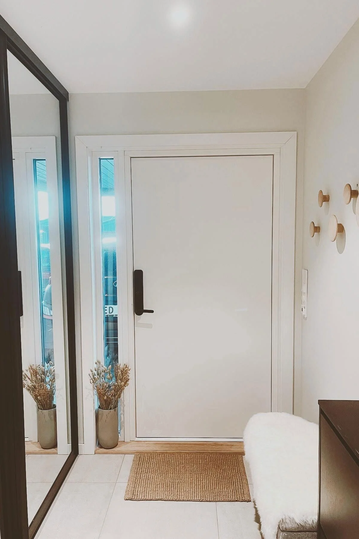 Ein skandinavisch gestalteter Flur mit einem Spiegel, einer Eingangstür und den Dots Wandhaken von Muuto an der Wand.