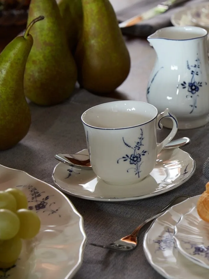 Weißes Porzellan-Teeservice mit blauem Blumenmuster, Birnen und Weintrauben auf einem Tisch.