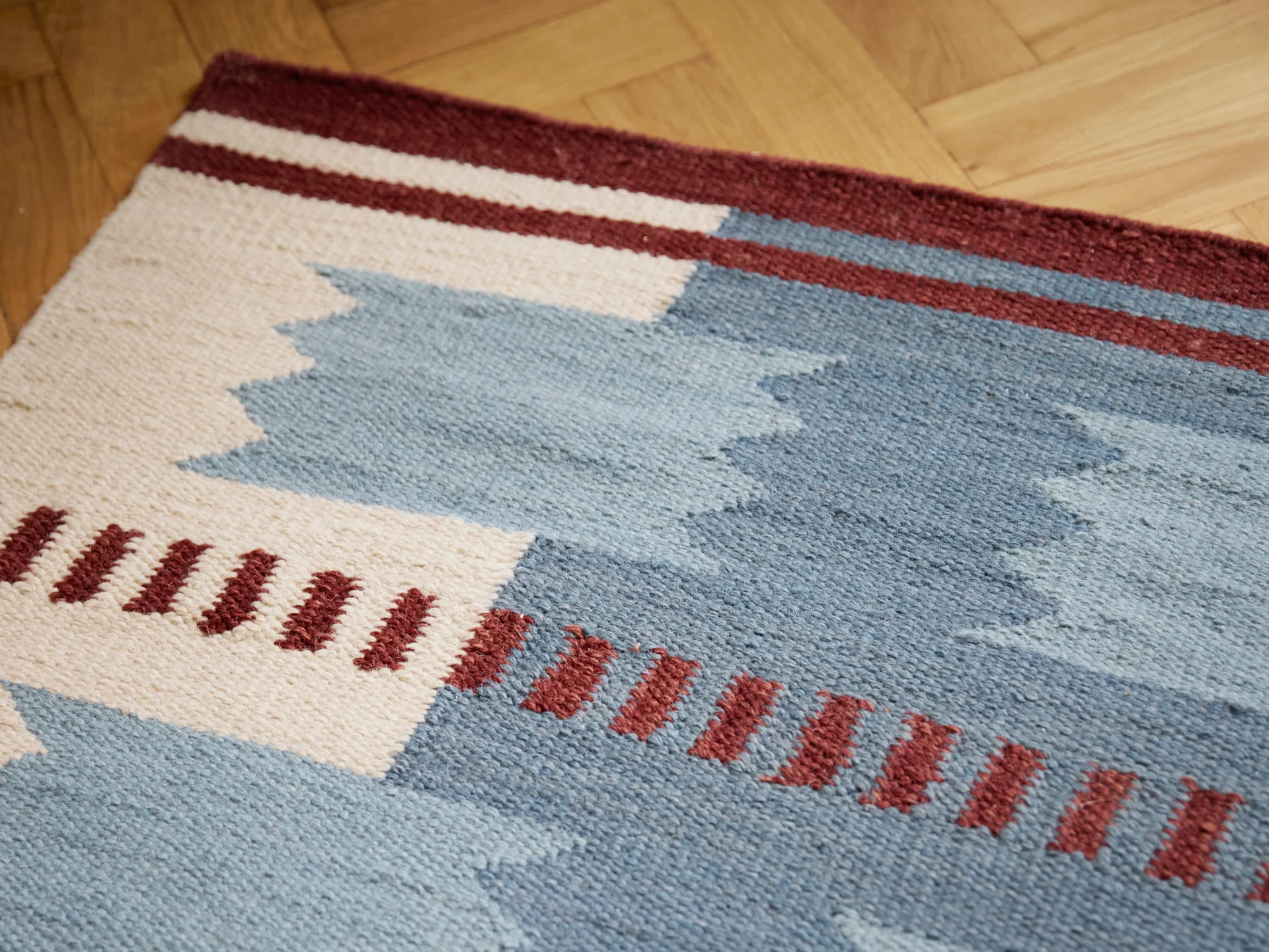 Gewebter Teppich mit geometrischen Mustern in Blau, Weiß und Bordeaux auf Holzboden.