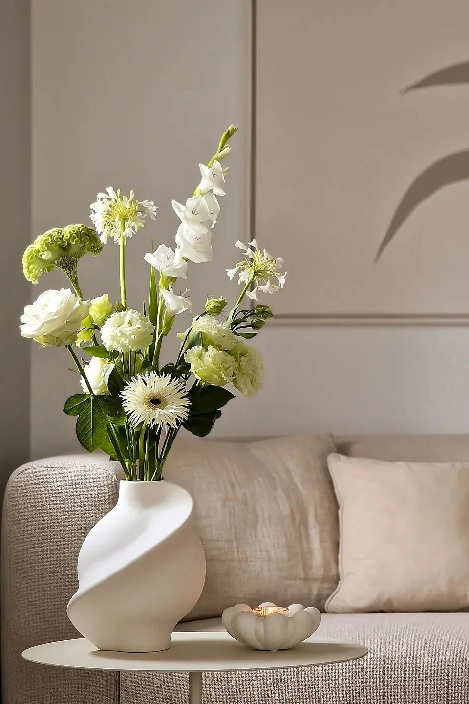In einem beigefarbenen Wohnzimmer ist ein Beistelltisch mit einer Vase mit Schnittblumen und einem Teelichthalter dekoriert.