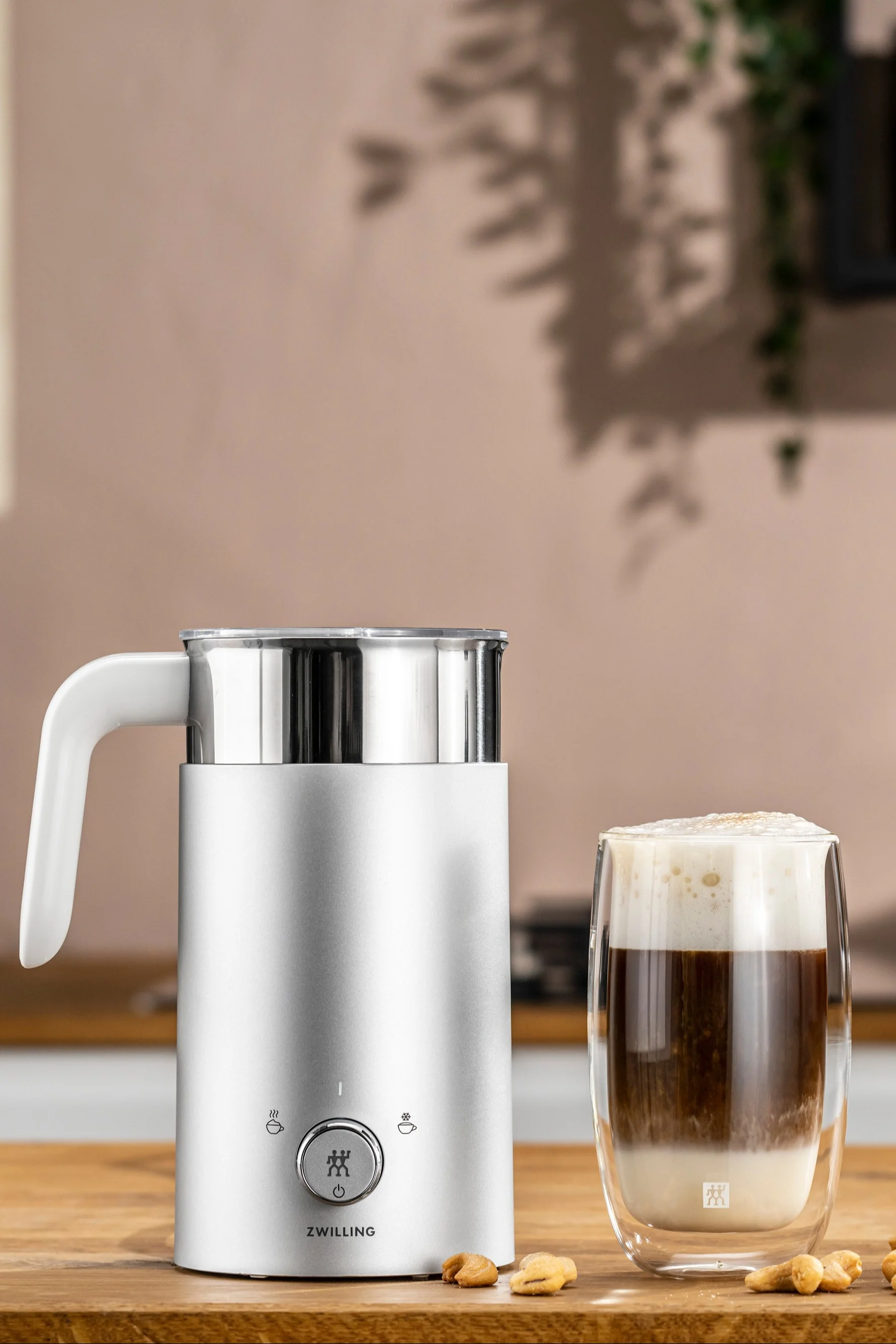 Ein elektrischer Milchaufschäumer ist das perfekte Geschenk für Väter, die einen guten Cappucchino zu schätzen wissen, da dieser die Arbeit ungemein erleichtert. Hier sehen Sie den Milchaufschäumer von Zwilling neben einer Tasse mit Cappucchino.