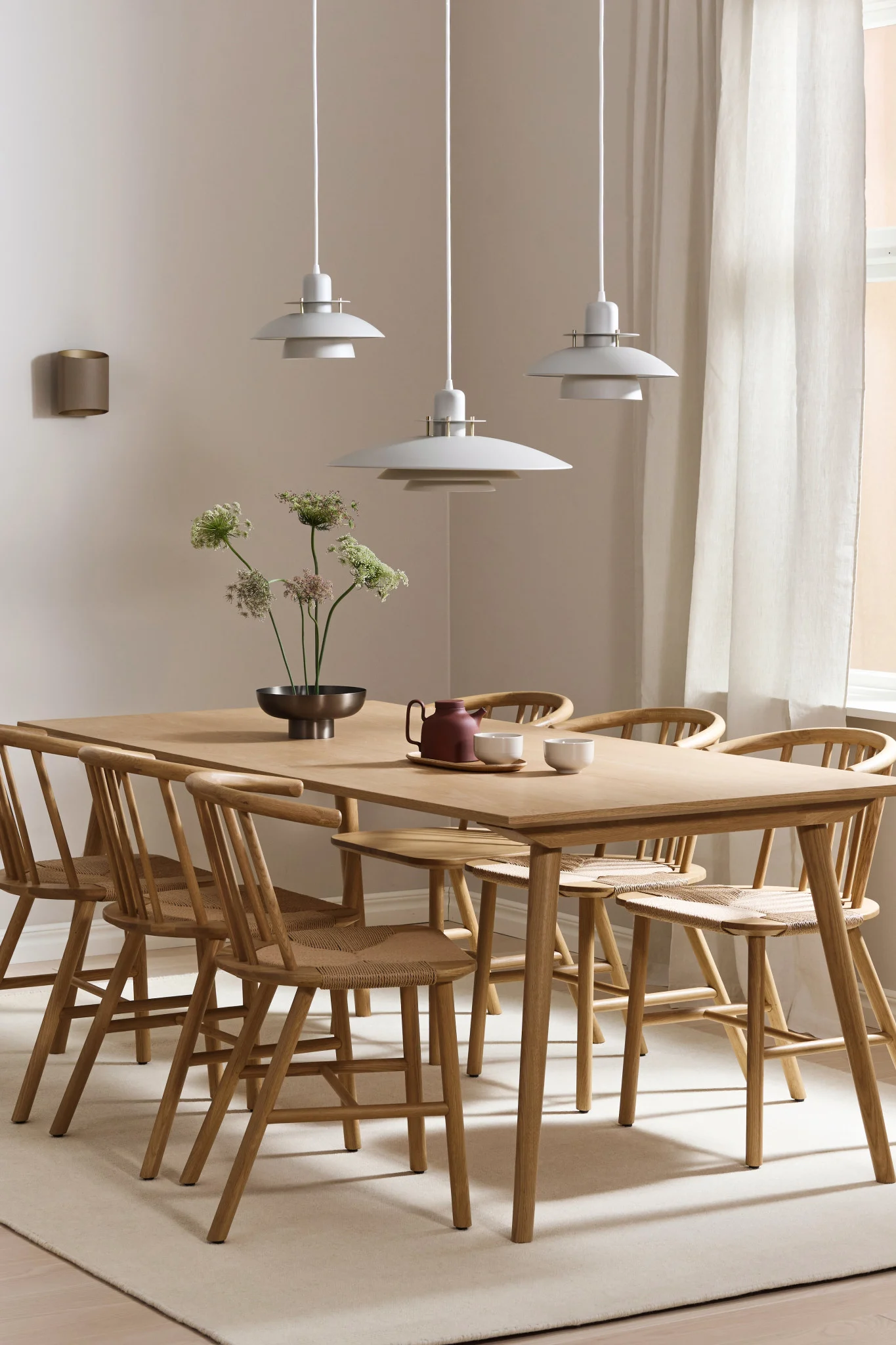 Esstischlampen: Die Picasso-Lampe hängt in einer Dreierreihe über einem rechteckigen Holztisch und die Sinne-Lampe an der Wand in einem Esszimmer.