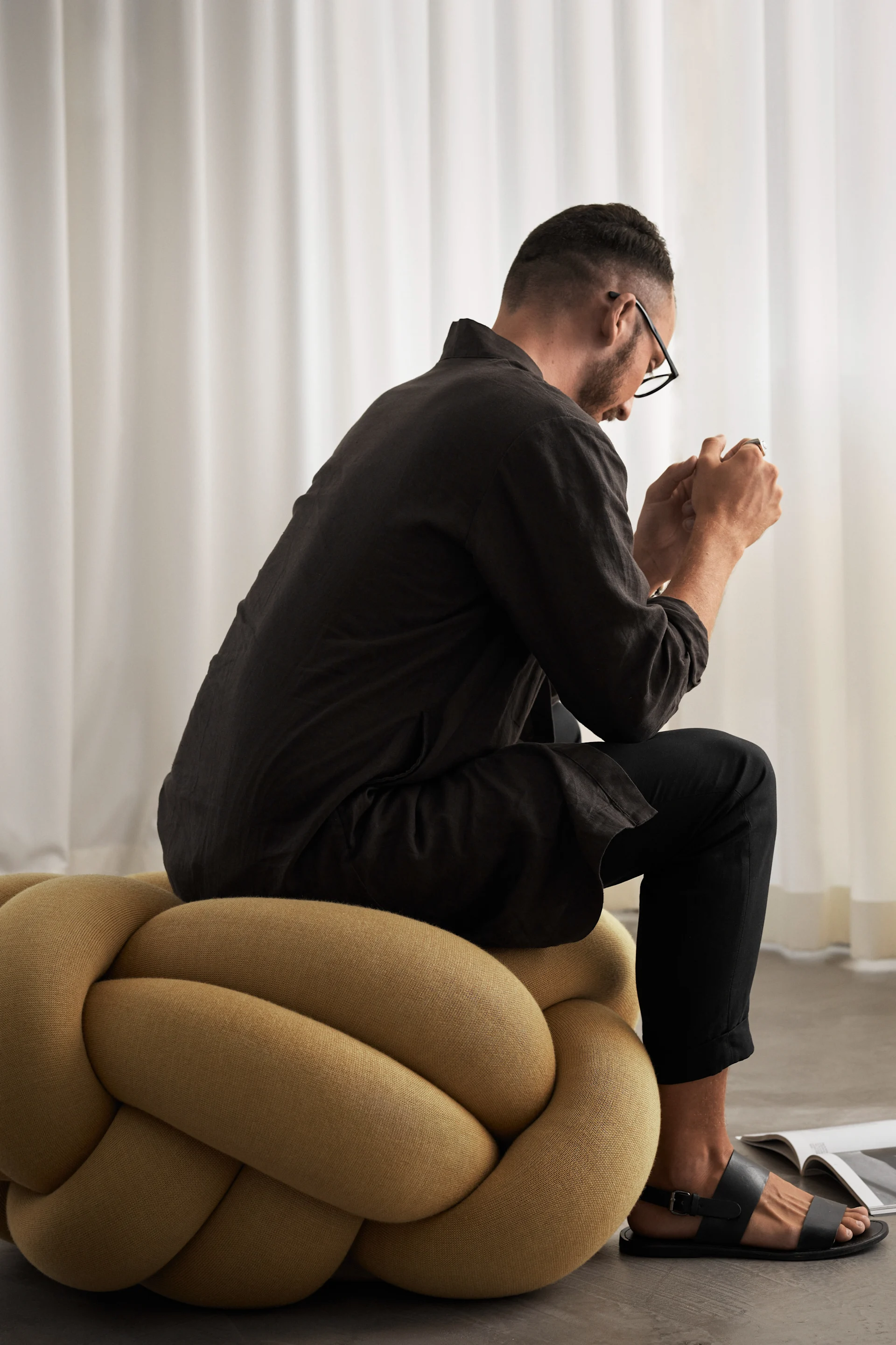 Ein Mann sitzt auf einem XL Knotenkissen in Gelb.