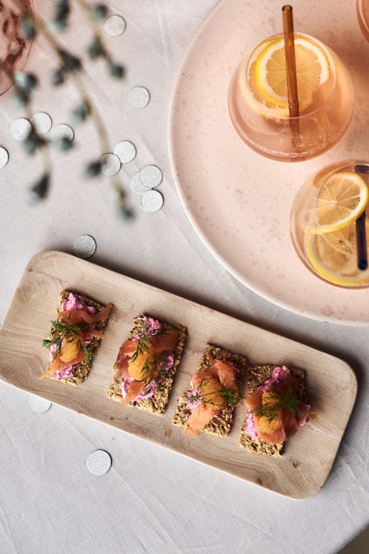 Kanapees mit Lachs und Rote Beete, eines der einfachen Vorspeisenrezepte für Ihre Silvesterparty serviert auf einem stilvollen Marmortablett von HK Living neben einem Champagner-Cocktail.