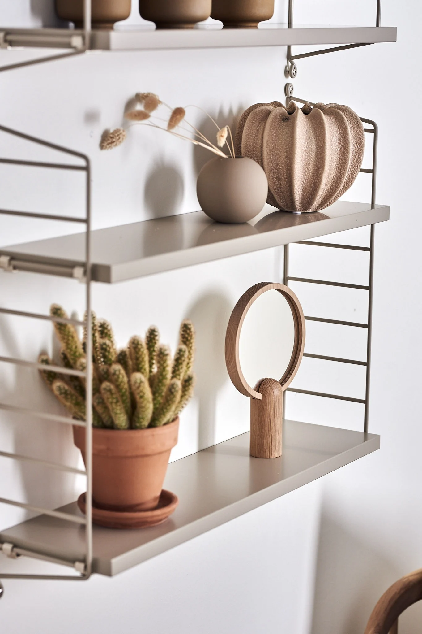 String Pocket Regal in Beige mit trendigen Einrichtungsdetails wie sandfarbenen Vasen.