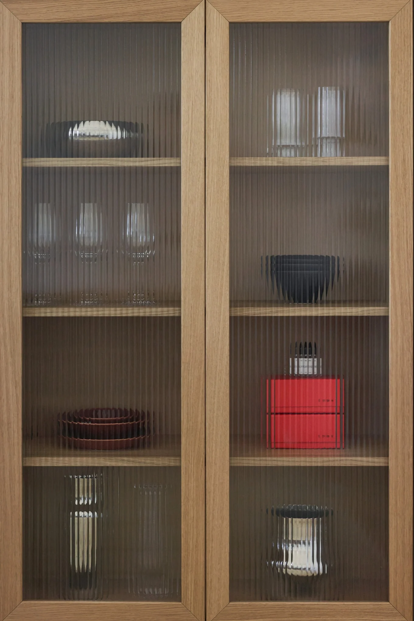 Holzschrank mit geriffelten Glastüren, der verschiedene Geschirr, Gläser und Dekorationsartikel auf Regalen zeigt.