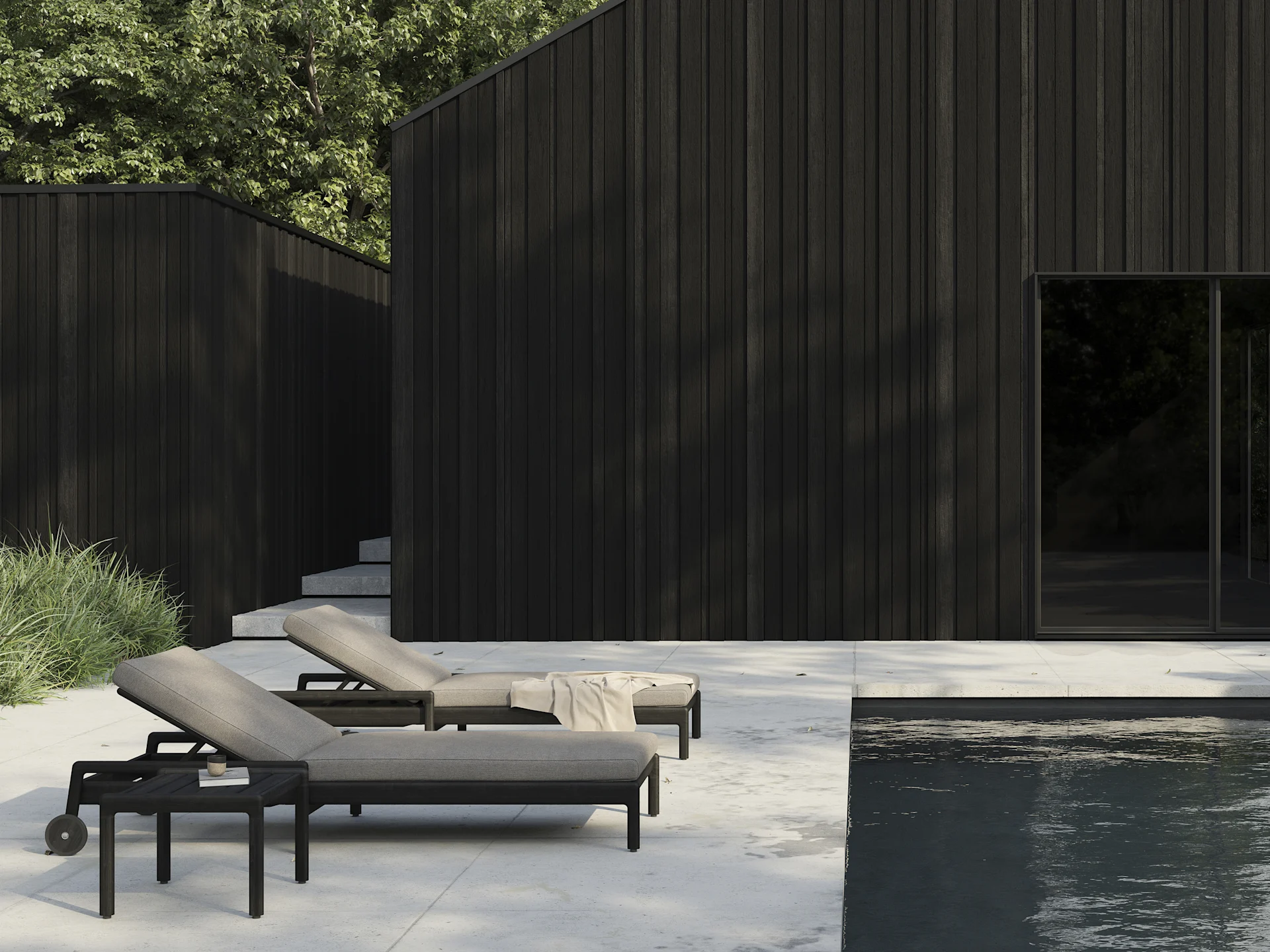 Zwei dunkle Sonnenliegen mit hellen Auflagen auf einer Terrasse am Pool, mit modernen dunklen Holzgebäuden im Hintergrund.