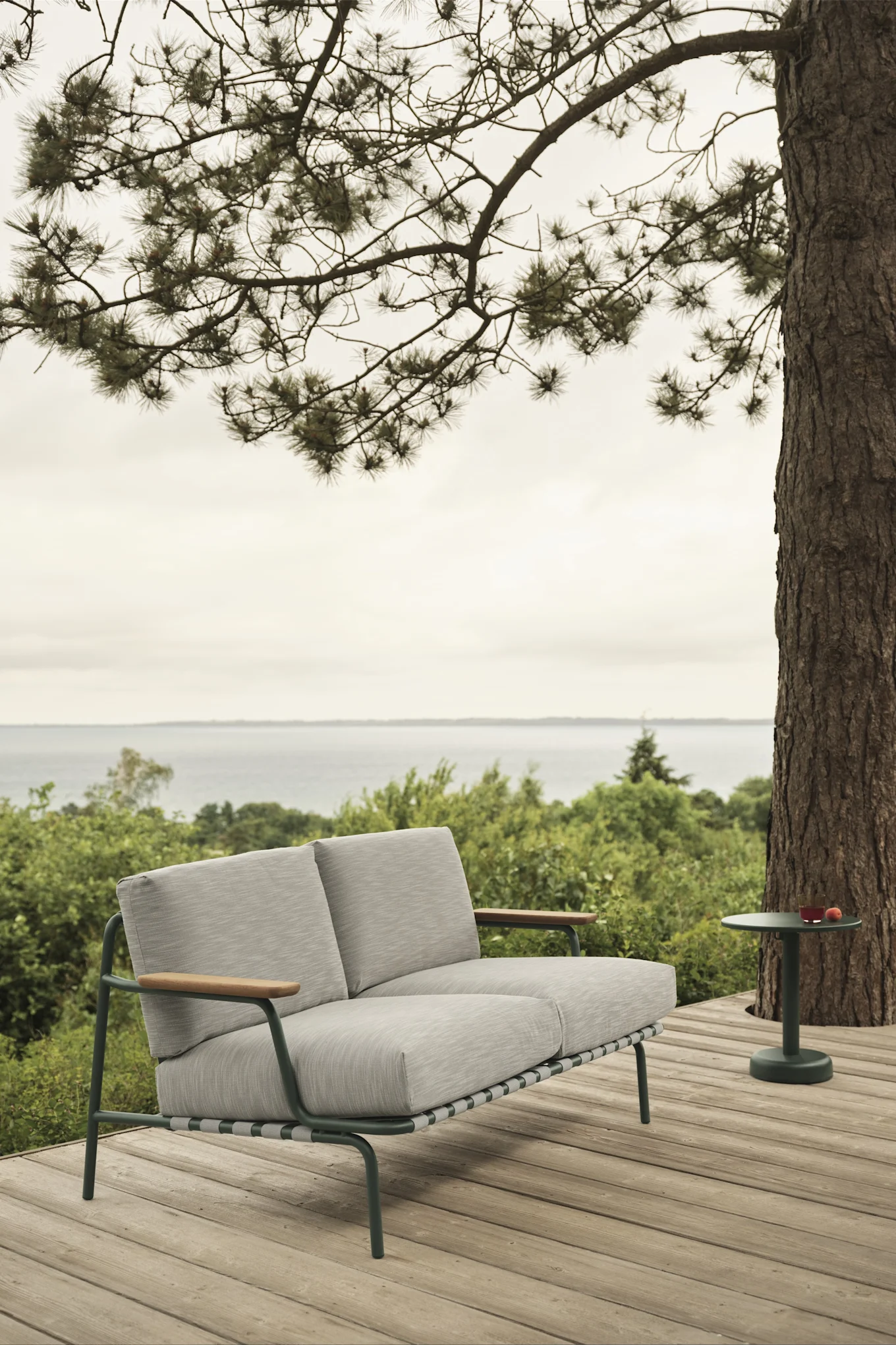 Das Outdoor-Sofa Settle von Muuto, hier auf einer Terrasse mit Blick aufs Wasser, bietet Platz und dank der dicken Kissen auch hohen Komfort - ein Muss unter den Gartenmöbel-Trends 2025.