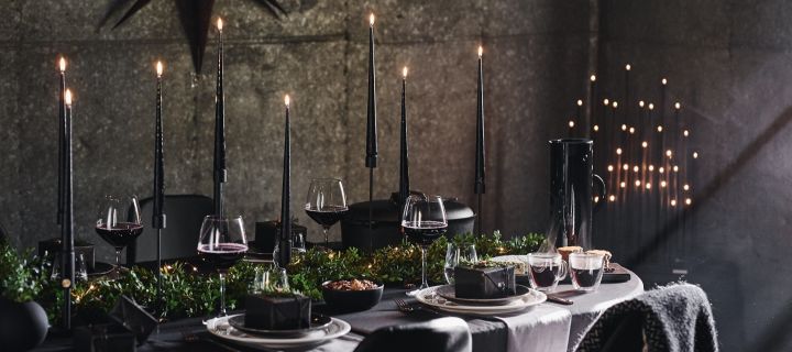 Eine dramatische Tischdekoration in Schwarz: Hier sehen Sie einen komplett schwarz gedeckten Tisch mit zahlreichen Kerzen.