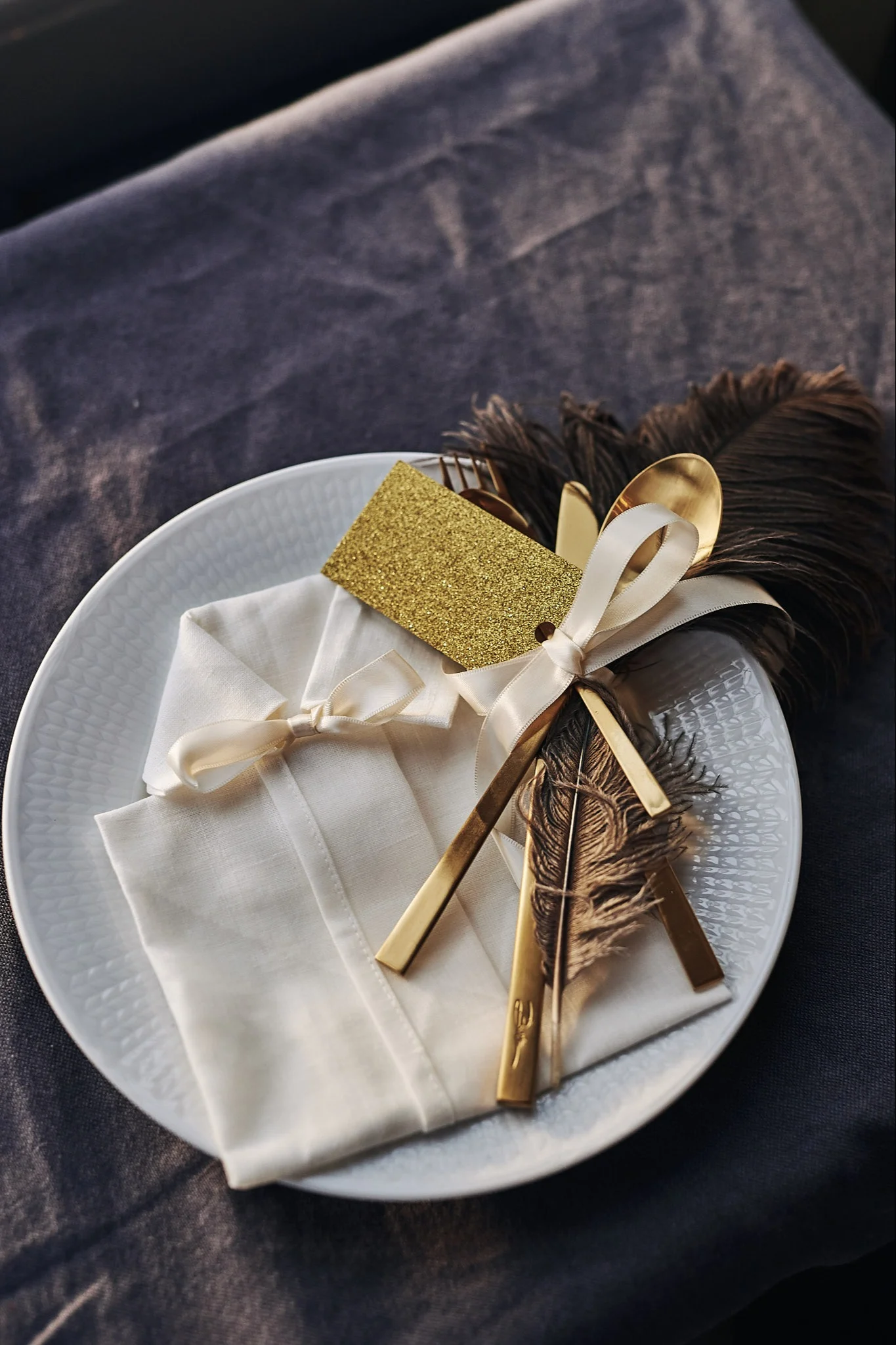 Eine Serviette in Form eines Hemdes liegt auf dem Teller mit Besteck, Tischkarten und einer dekorativen Feder.