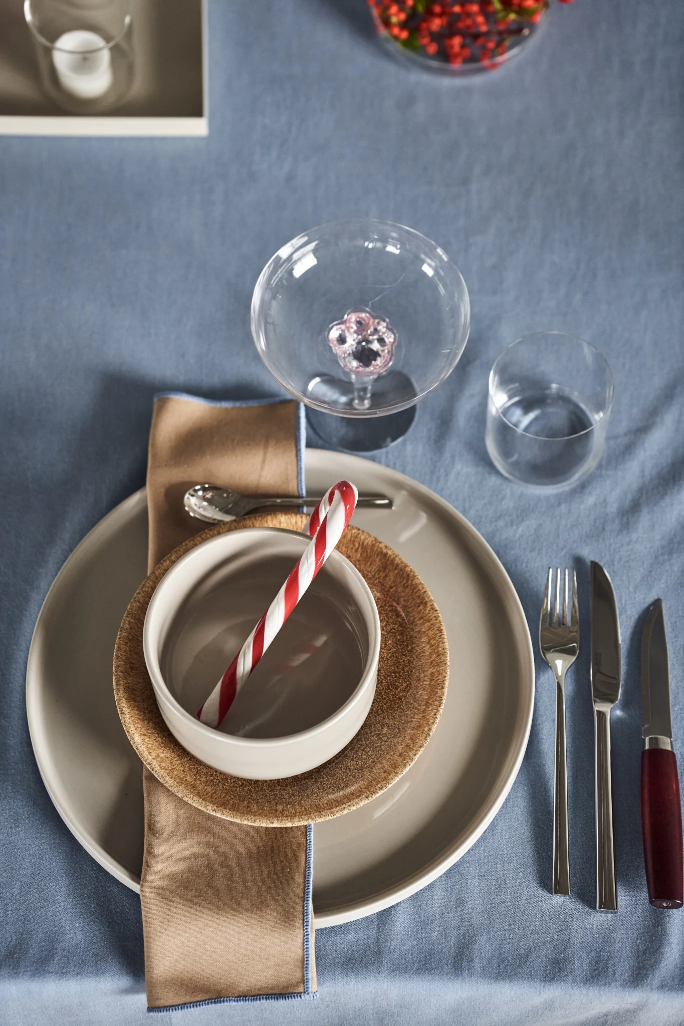 Ein weihnachtlich gedeckter Tisch mit Geschirr aus der Pilar-Kollektion von Blomus und einer Zuckerstange.