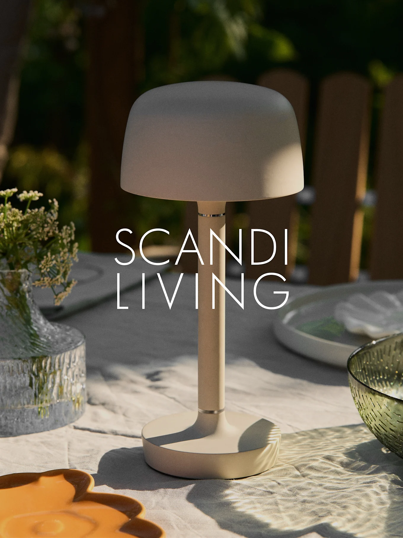 Eine beigefarbene moderne tragbare Tischlampe auf einem Gartentisch mit Blumenvase und Geschirr. Text: "SCANDI LIVING".