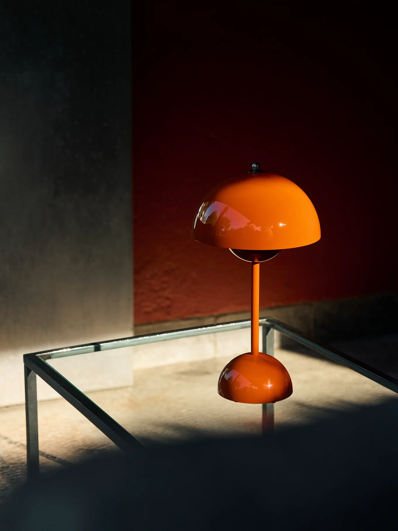 Orangefarbene pilzförmige Tischlampe auf einem Glastisch, die Grün reflektiert.