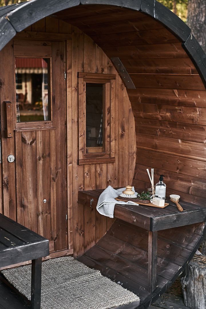 Setzen Sie einen Besuch in einer schwedischen Sauna unbedingt auf Ihre Summer Bucket List. Hier sehen Sie eine Holzsauna mit einer Sammlung von Kerzen und Bürsten im Freien.