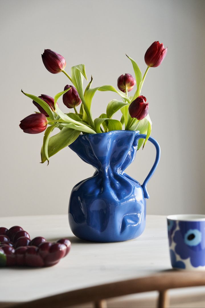 Farbtrends 2024: Zu den Trendfarben 2024 gehören auch verschiedene Blautöne. Hier sehen Sie die blaue Crumple Vase von Byon mit roten Tulpen darin.