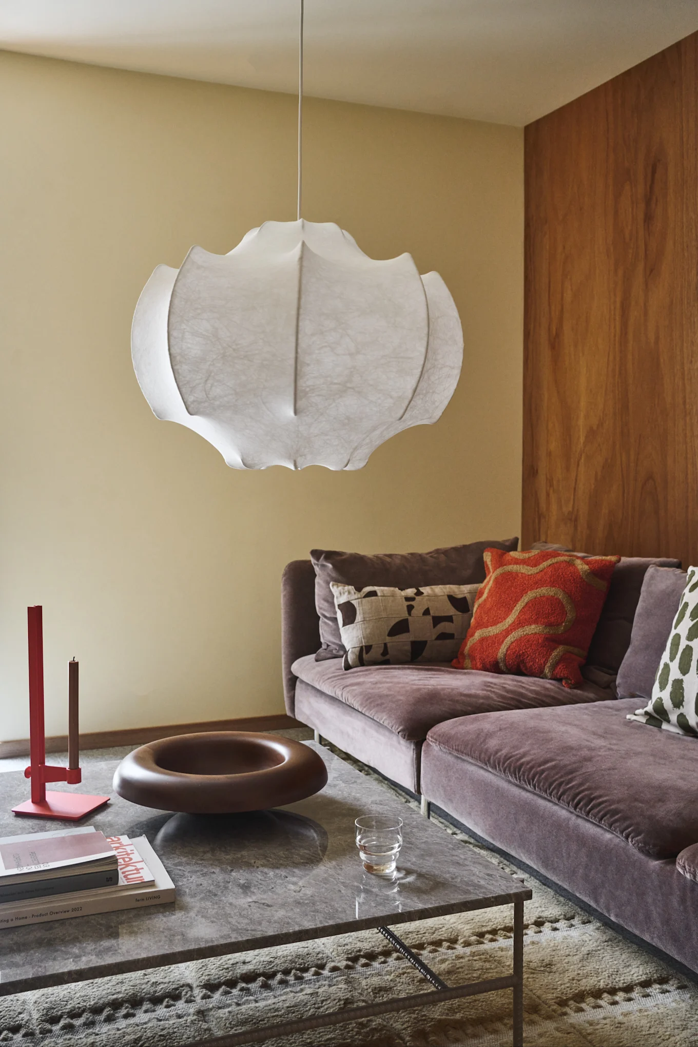 Modernes Wohnzimmer mit großer weißer Pendelleuchte, violetter Samtsofa mit gemusterten Kissen und Marmor-Couchtisch.