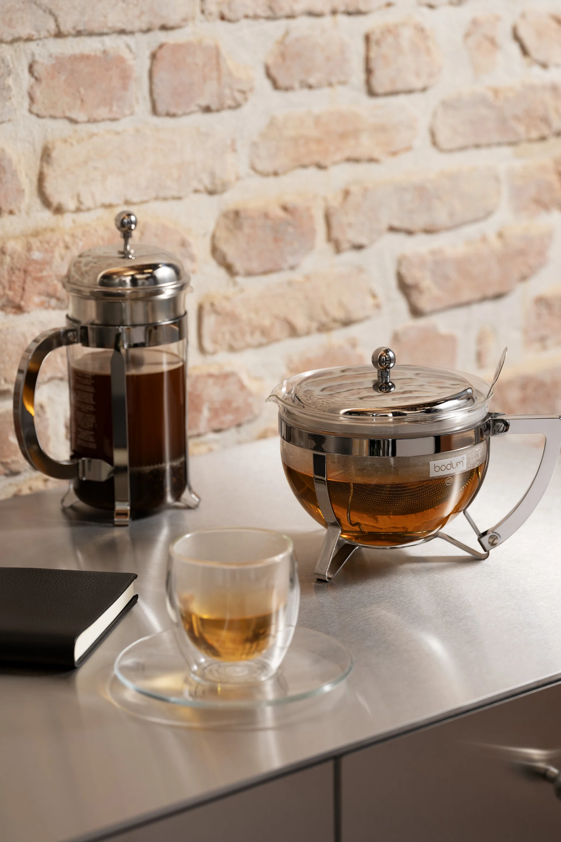 Geschenk zum Valentinstag: Hier stehen eine French Press und eine Teekanne aus der Chambord-Kollektion von Bodum neben einer Bistro-Tasse mit Tee auf einer Küchenanrichte.