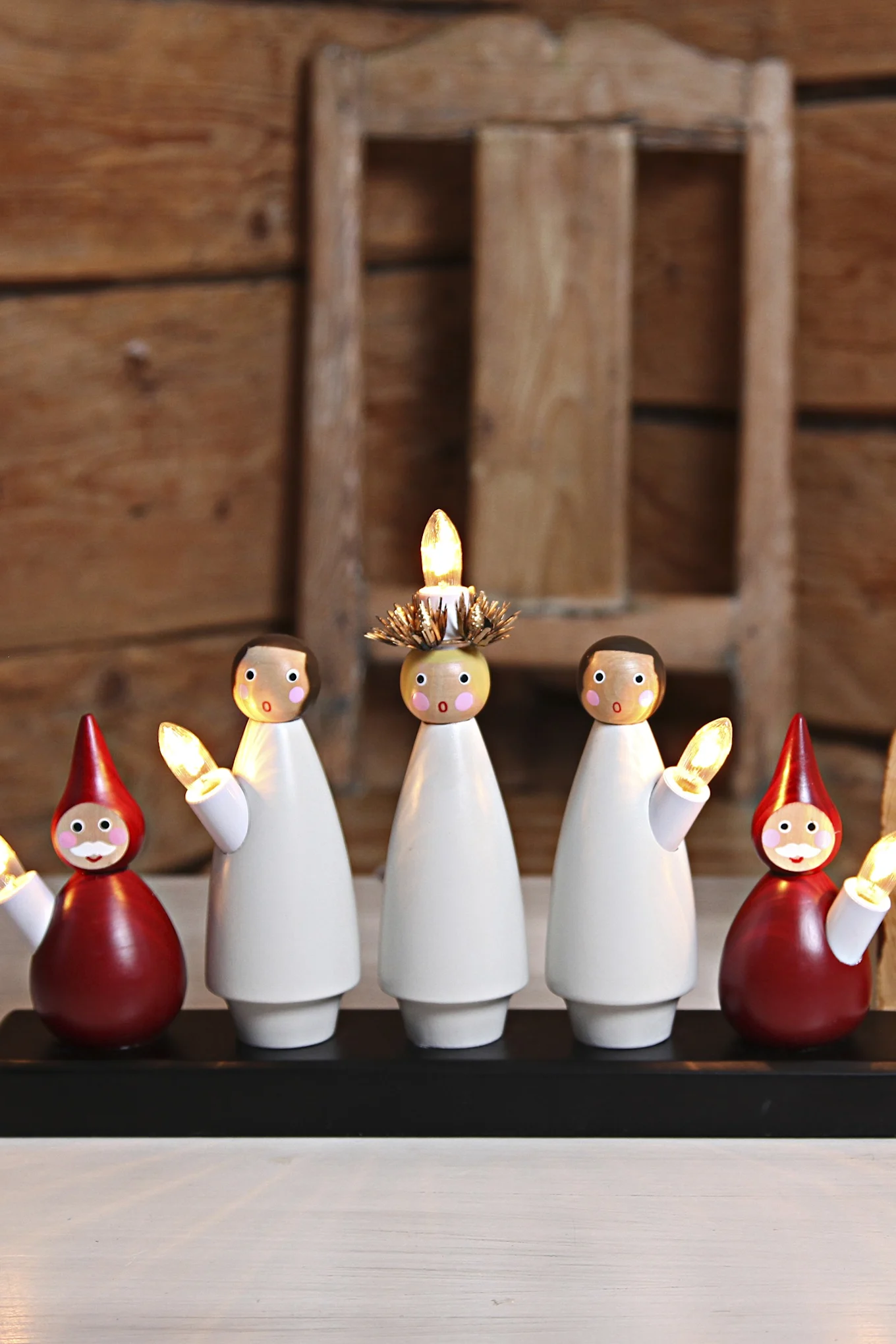 Fünf weiße Holz-Schneemannfiguren mit leuchtenden Lichtern auf einem weißen Sockel, neben einem Weihnachtsbaum.