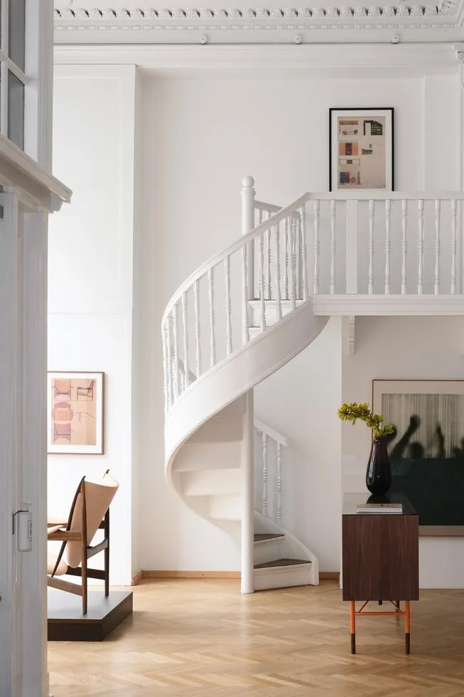 Heller, moderner Innenraum mit weißer Wendeltreppe, hellem Parkettboden, Konsolentisch mit Vase und Kunstwerken.