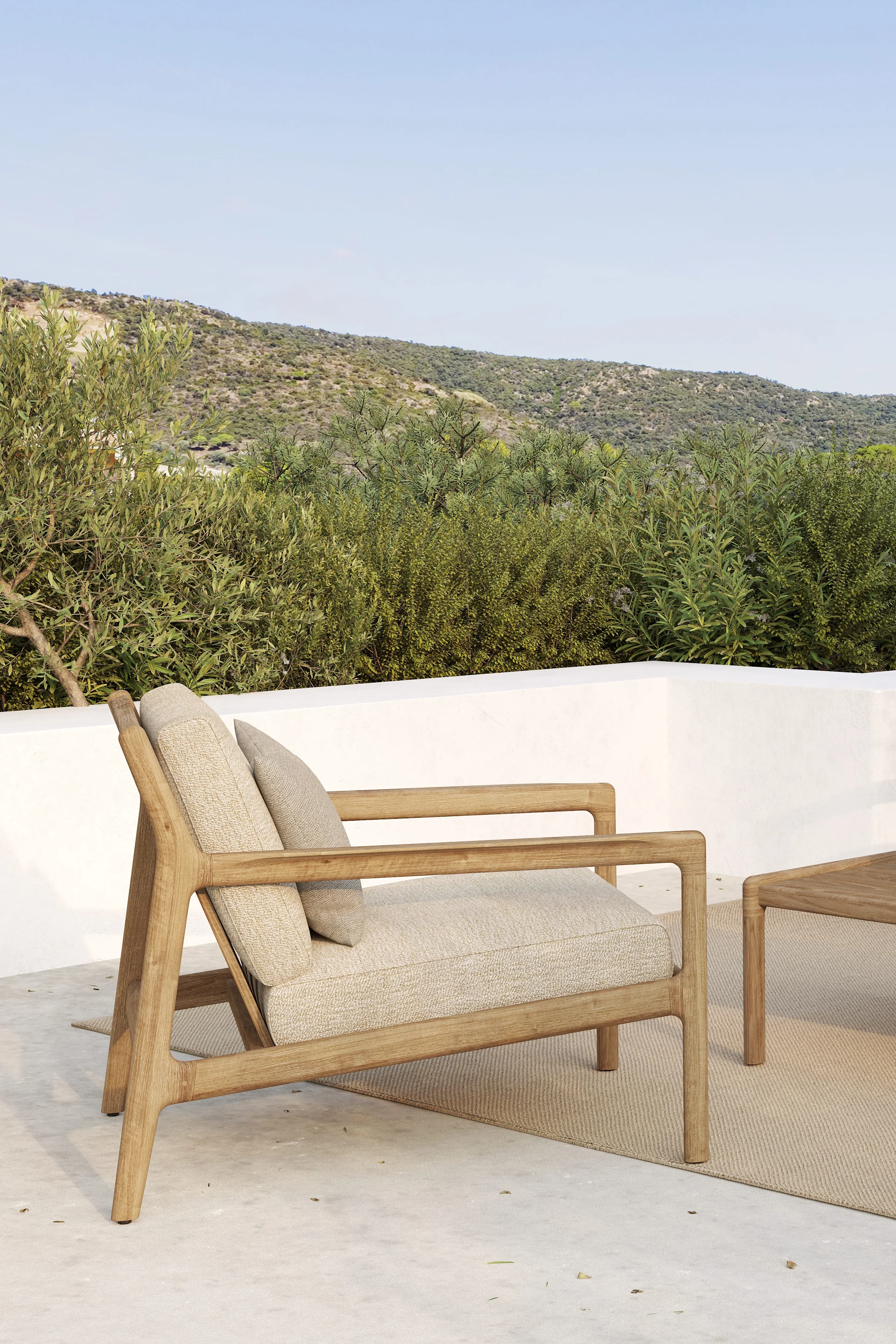 Outdoor-Holzsessel mit hellen Kissen auf einer Terrasse, vor grünen Hügeln und blauem Himmel.