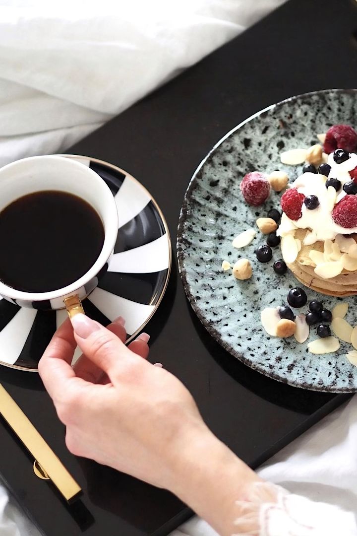 Ein Serviertablett für ein gemeinsames Frühstück im Bett ist eine tolle Hochzeitsgeschenk-Idee. Hier sehen Sie das schwarze Hilke Collection Tablett in einem Bett mit Pancakes und einer Tasse Kaffee darauf.