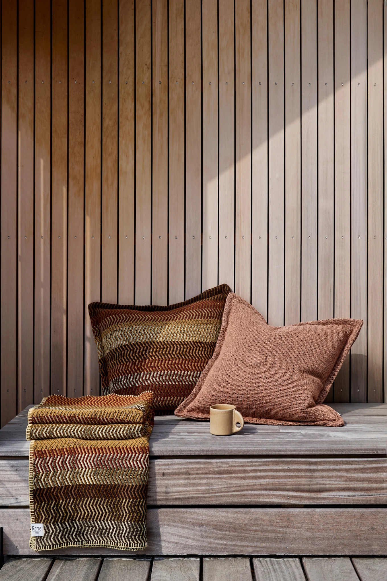 Boho-Balkon dekorieren: Für den Boho-Stil sind die richtigen Farben entscheidend - hier sehen Sie das Fri-Kissen von Røros Tweed in Braun-Rot-Gelbtönen auf einem Balkon.