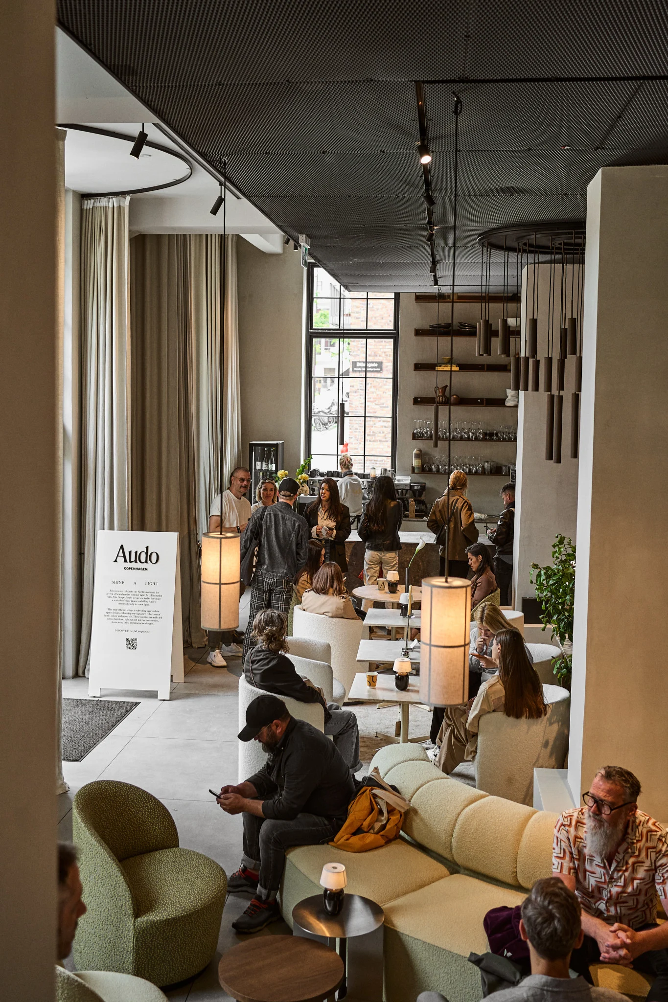 Eine schicke, moderne Lounge mit Menschen, die sich unterhalten, auf hellen Sofas und Sesseln sitzen und stehen.