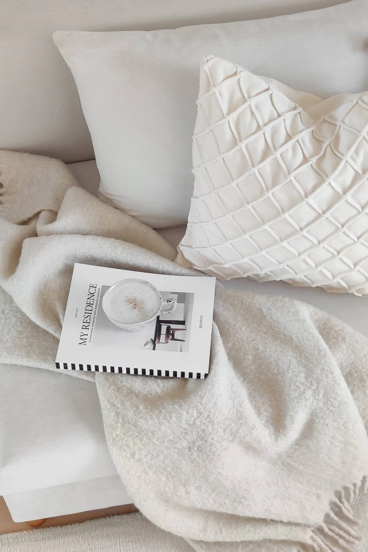 Valentinstagsgeschenke: Auf einer weißen Couch stehen zwei weiße Kissen von Chhatwal & Jonsson, die Ralph-Decke von Klippan Yllefabrik, ein Buch und eine Tasse Kaffee.