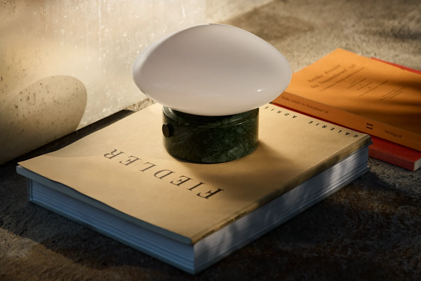 Eine dunkelblaue, pilzförmige Tischlampe mit silbernem Stiel und Fuß steht auf einem reflektierenden Tisch neben einem Stapel Bücher.