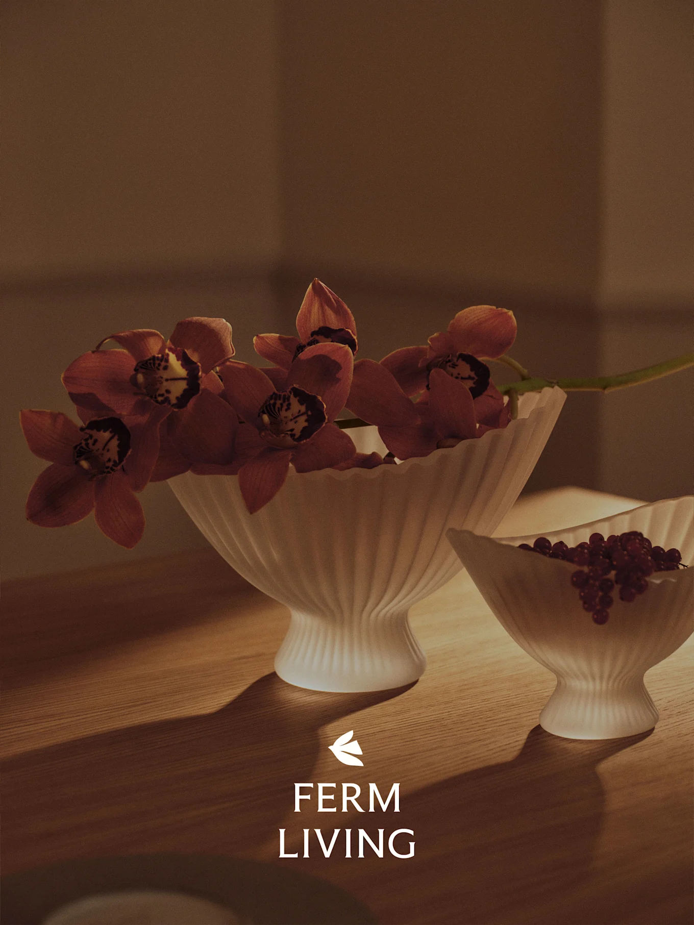 Zwei gerillte weiße Schalen auf einem Holztisch, eine mit roten Orchideen, die andere mit roten Beeren, in warmem Licht.