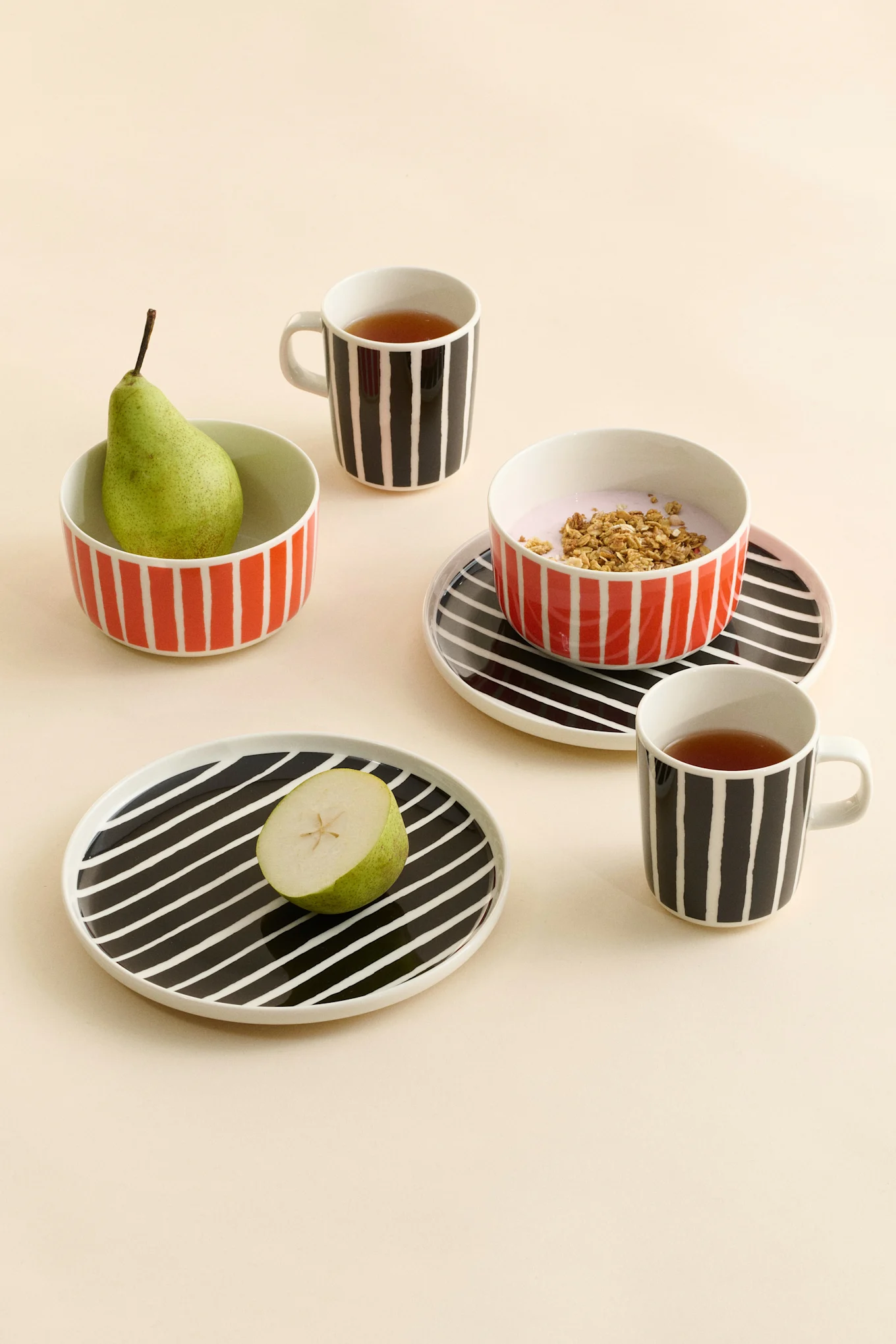Gestreifte Keramikbecher mit Tee, Schalen mit einer Birne und Joghurt mit Müsli sowie Teller mit einer halben Birne.