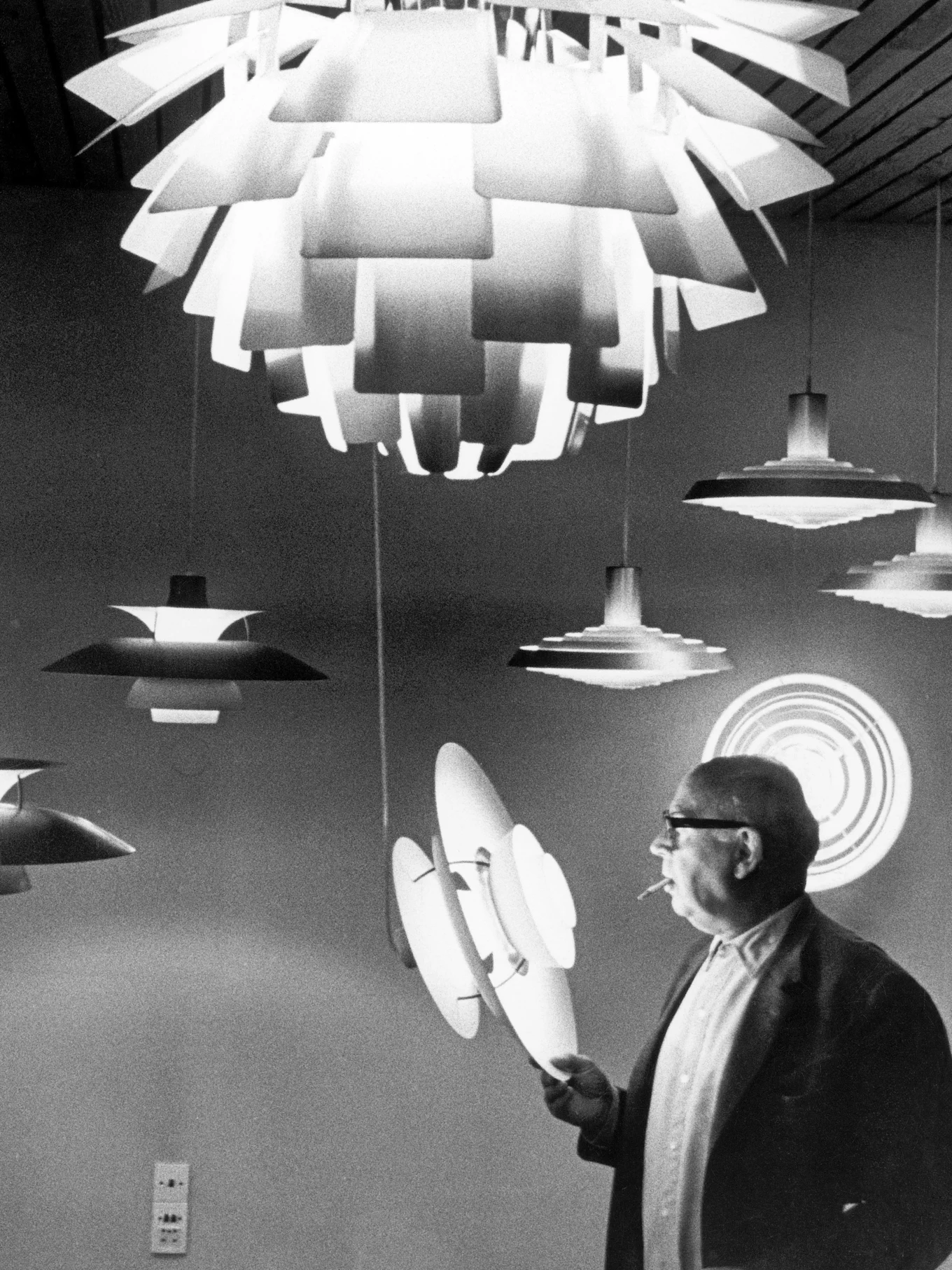 Mann mit Brille und Zigarette inspiziert mehrere geschichtete, moderne Lampen in Schwarz-Weiß.