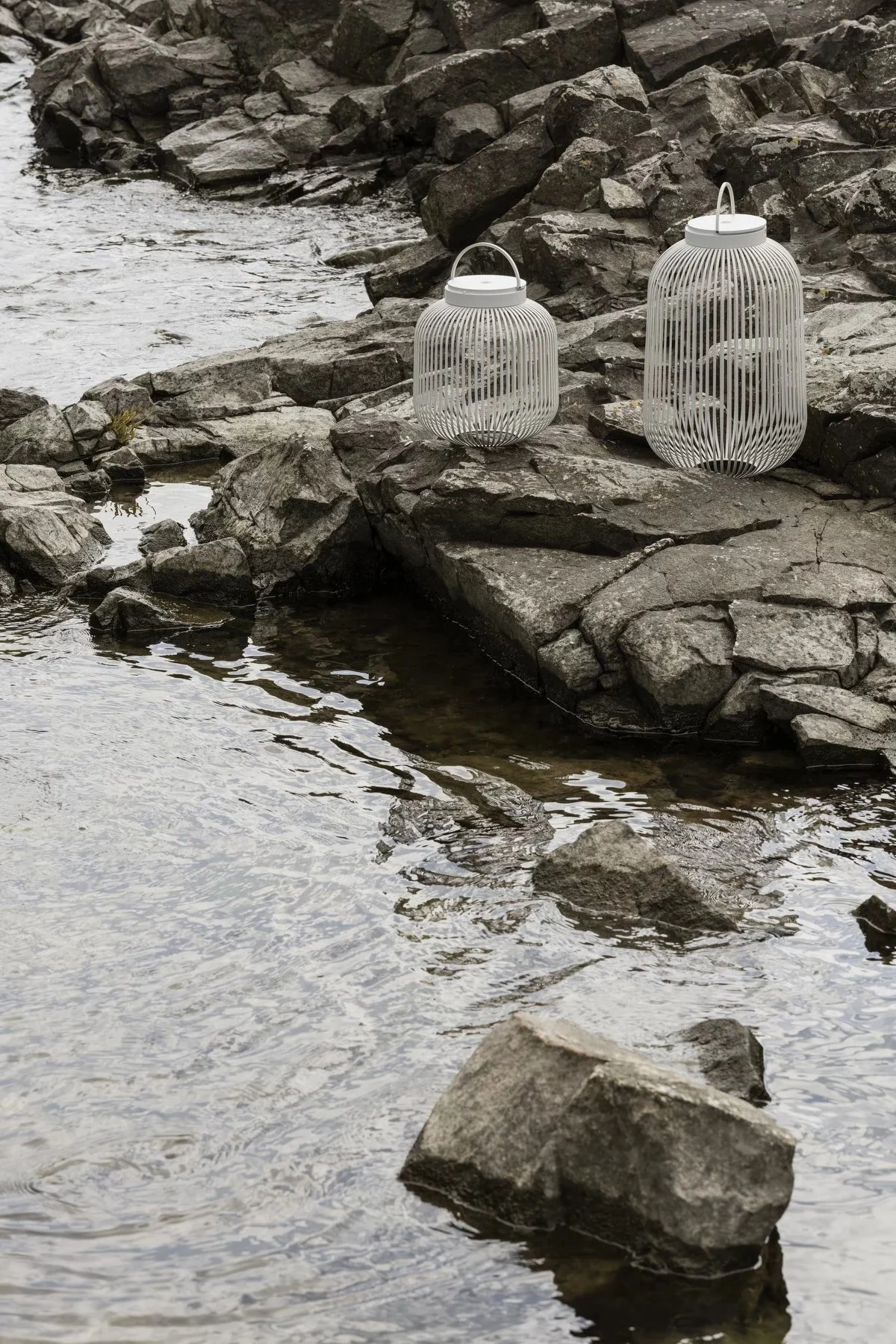 Laternen und Windlichter für draußen – hier sehen Sie die Lito-Laterne von Blomus in Weiß in verschiedenen Größen auf Felsen stehen.